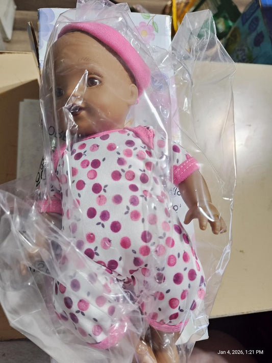 Doll with pink polka dot outfit, packaged in plastic, featuring a smiling face.