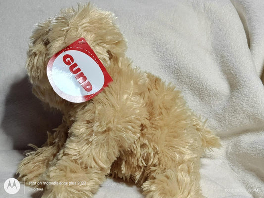 GUND plush teddy bear with fluffy fur and a red tag, sitting on a soft surface.