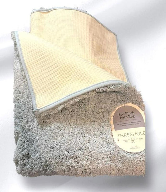 Threshold plush bath rug in soft gray color with textured surface and beige border.