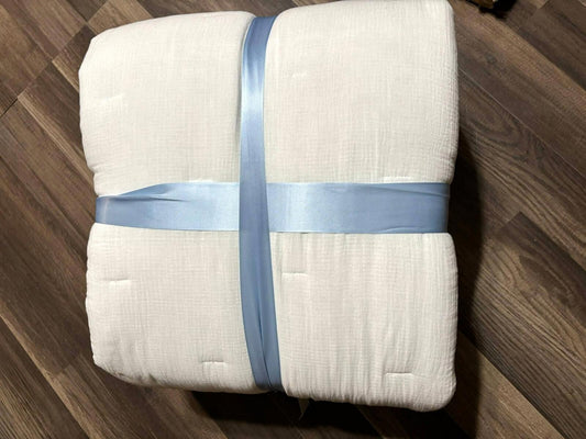 White quilted blanket with blue ribbon tied around it, showcasing a soft texture.