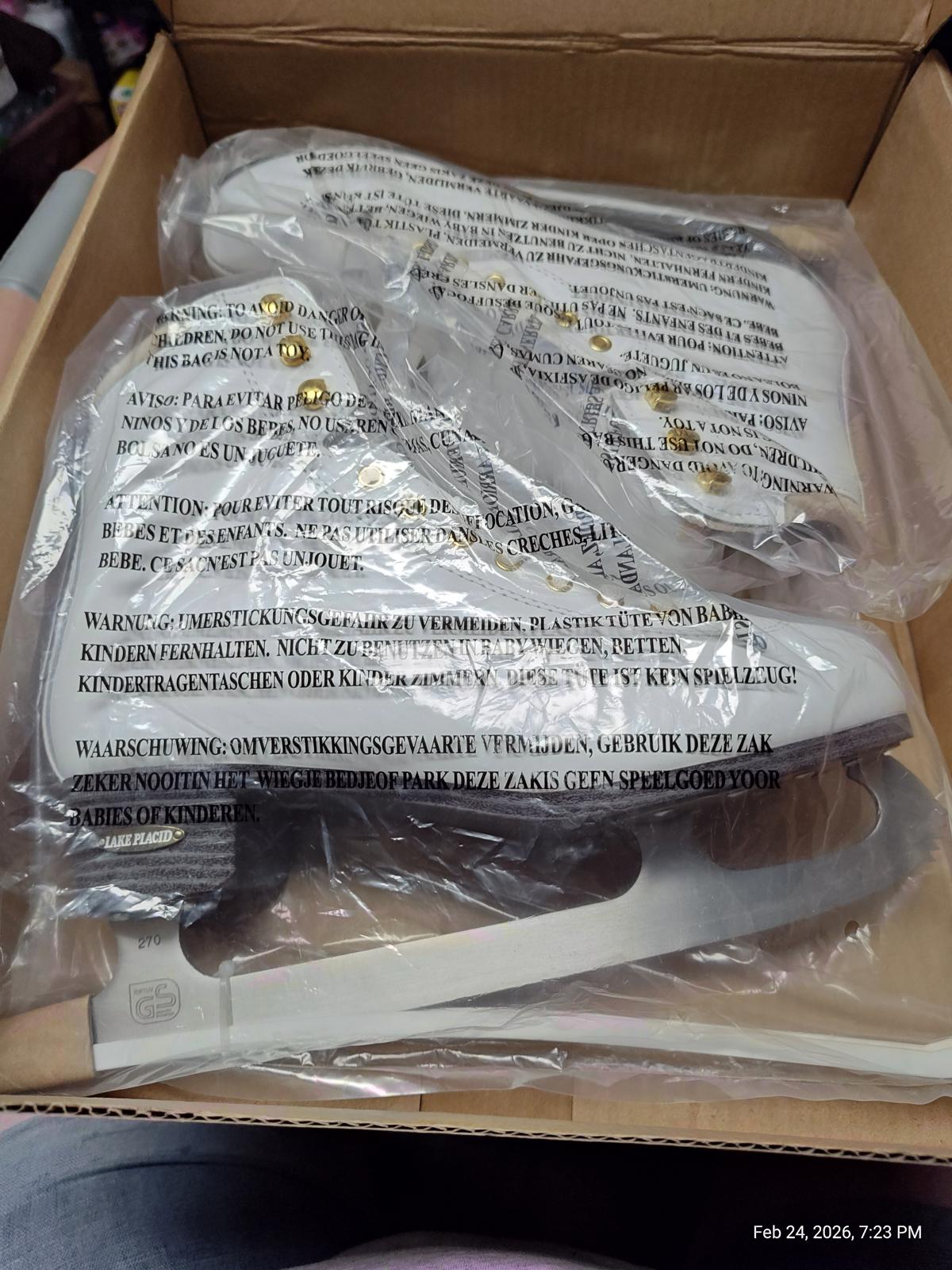 White ice skates with gold accents in a box, featuring protective packaging.