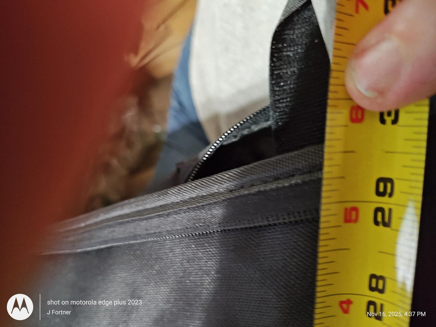 Measuring the zipper of the black messenger bag with a tape measure.