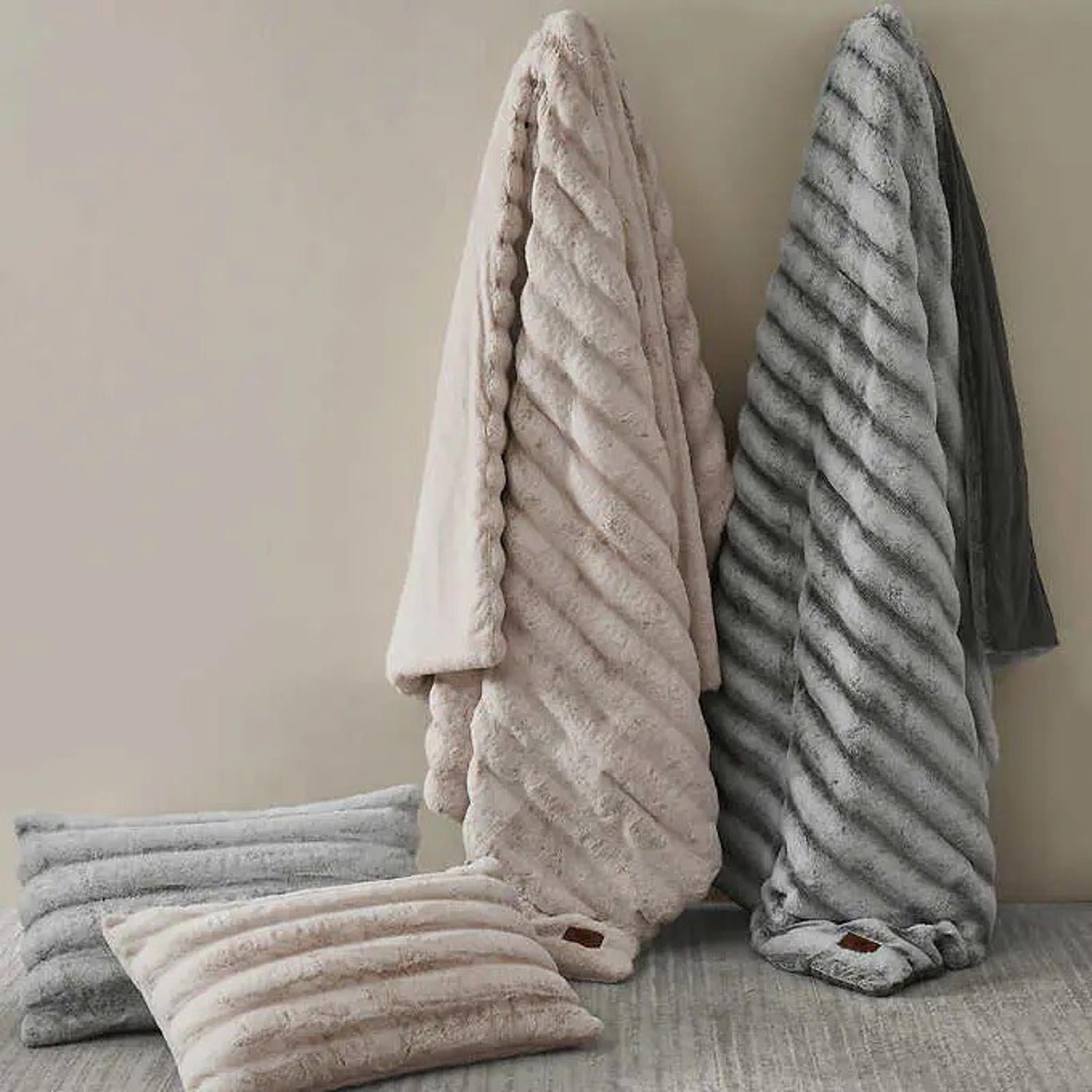 Cozy faux fur throw blanket in blush and gray colors, draped elegantly with matching pillows.