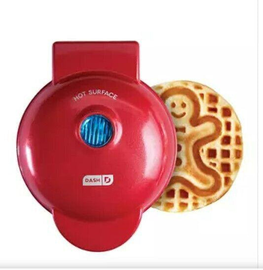 DASH red waffle maker with a gingerbread man design waffle beside it.