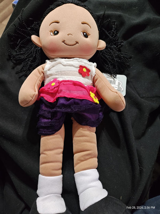 Doll with black hair wearing a colorful outfit featuring a white top and purple skirt.
