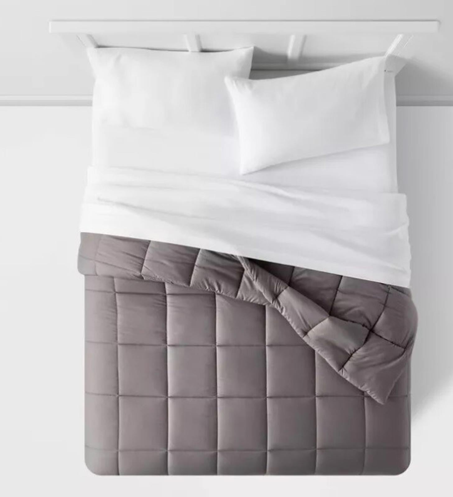 Gray quilted bedspread with white bedding on a neatly made bed.