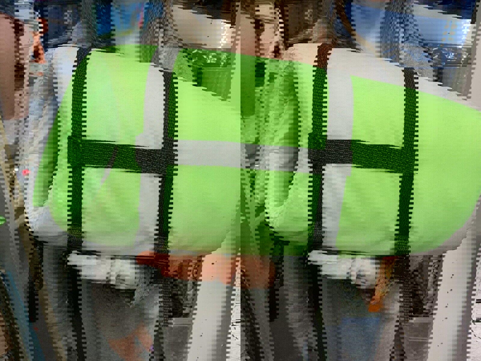 Green sleeping bag with black straps held by a person, ideal for camping and outdoor adventures.