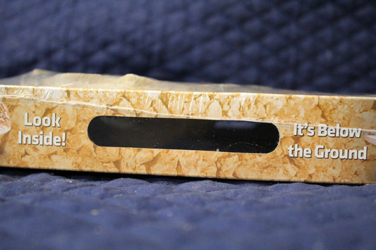 Product packaging for It's Below the Ground with a peek-through window and textured design.