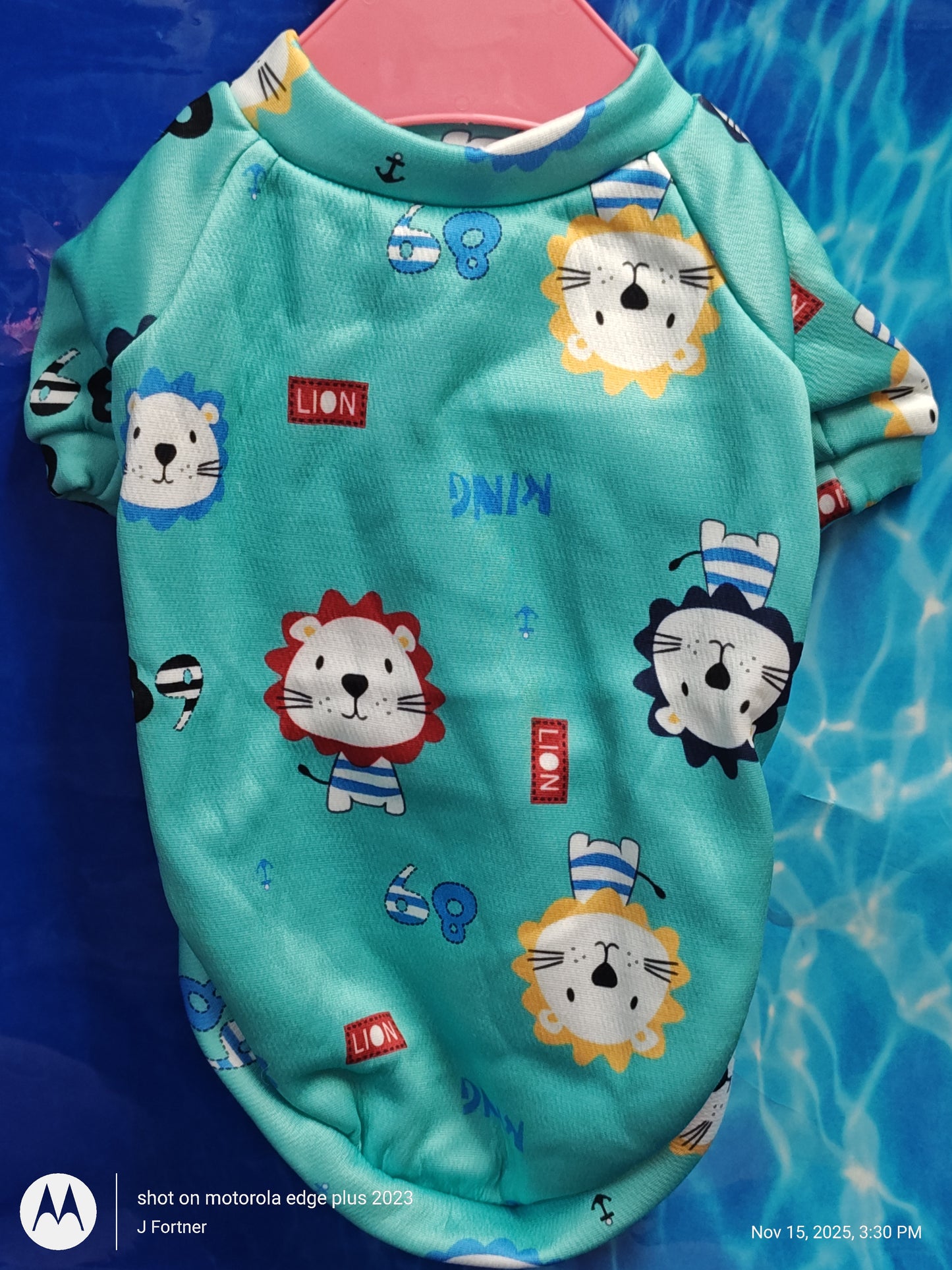 Lion Print Dog Shirt features colorful lion designs on a turquoise background.
