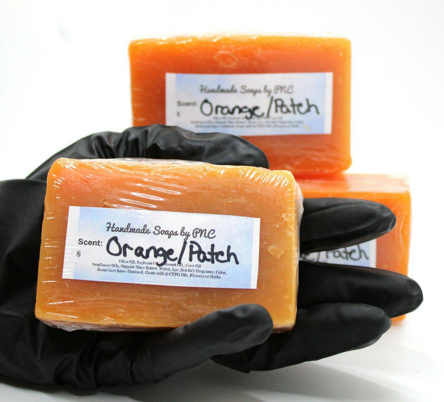 Orange/Patch soap bars displayed in a hand with a black glove, showcasing their vibrant color and packaging.
