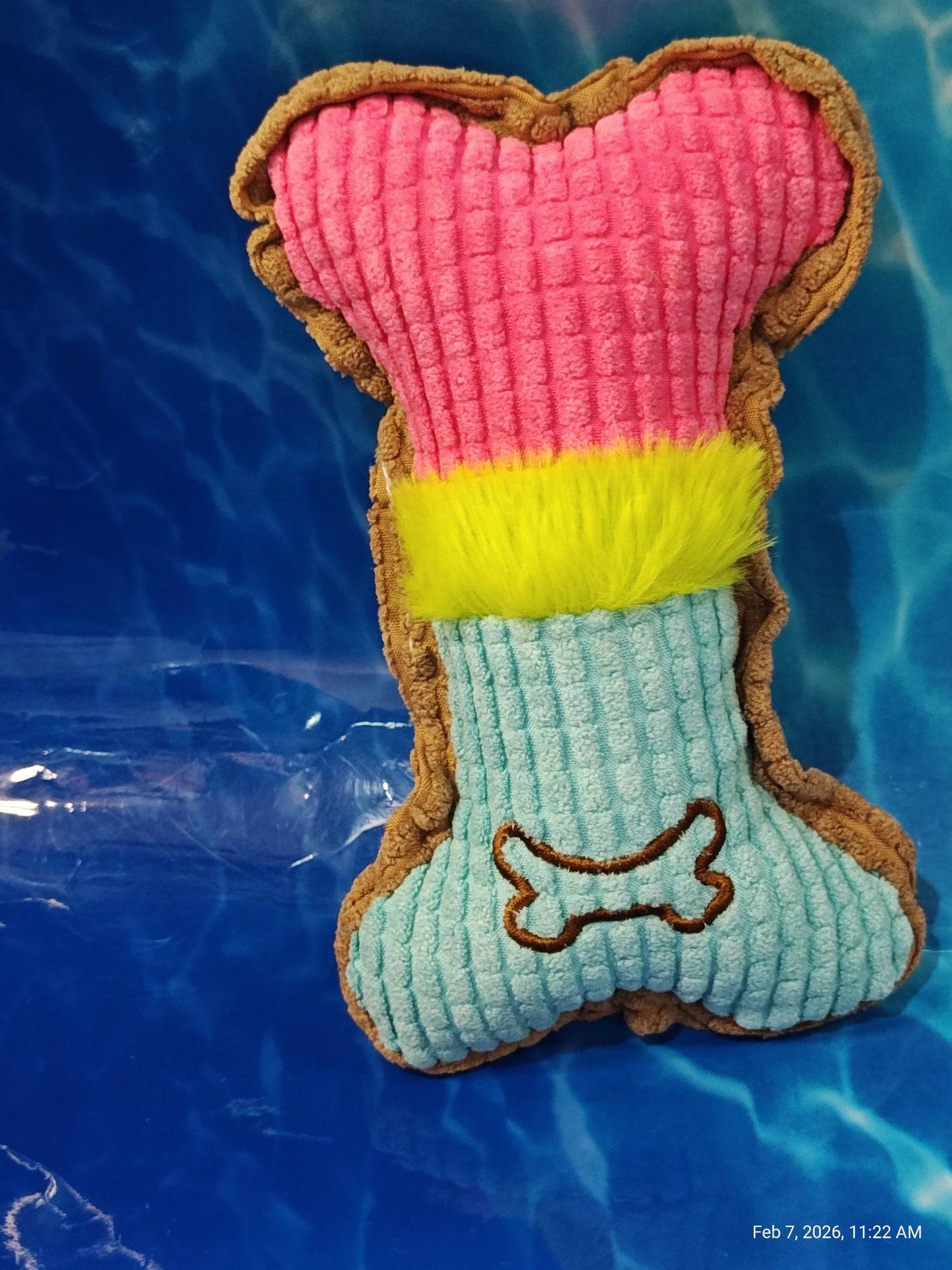 Plush Dog Toy Bone in pink, yellow, and blue colors with a textured surface.