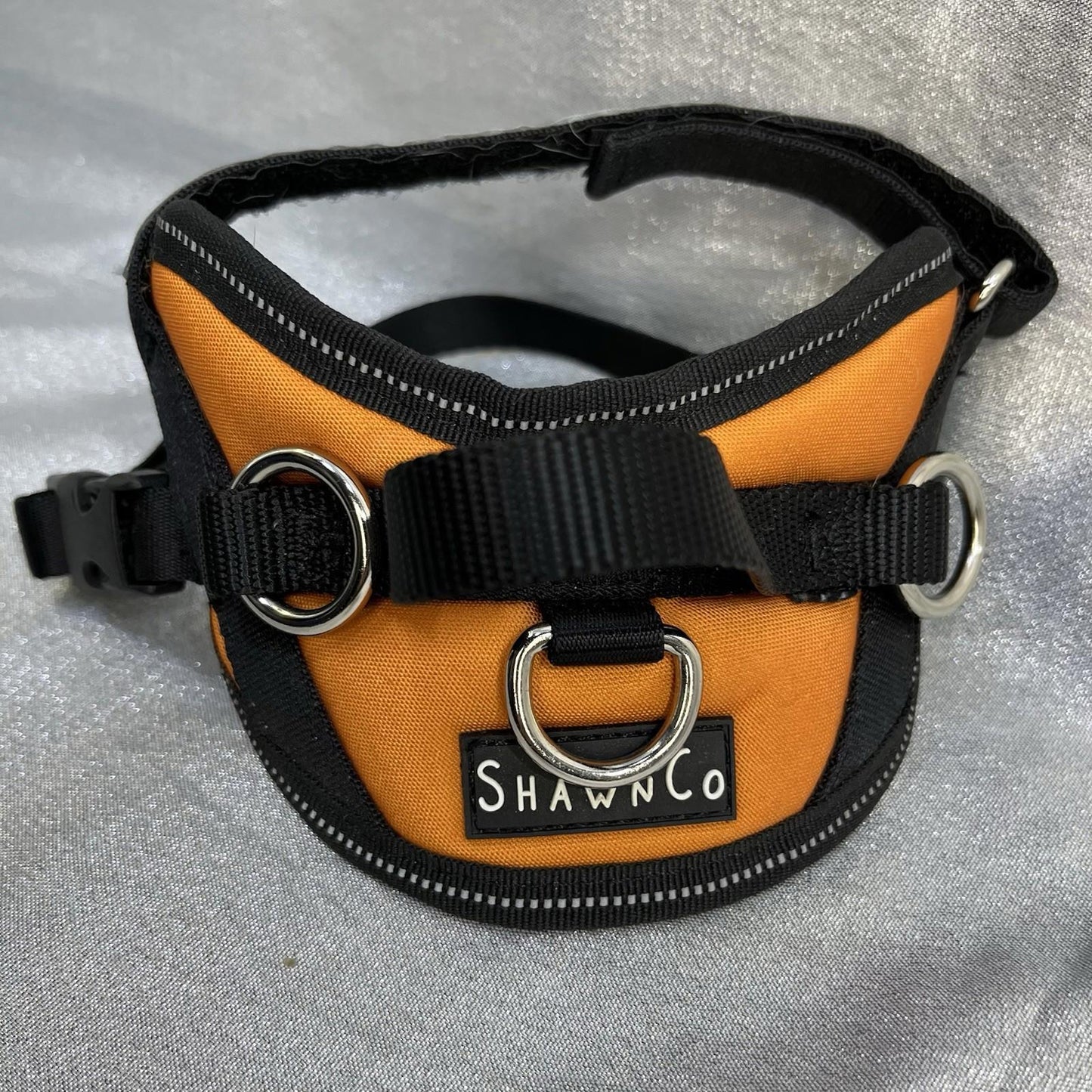 ShawnCo dog harness in orange and black with adjustable straps and metal rings.