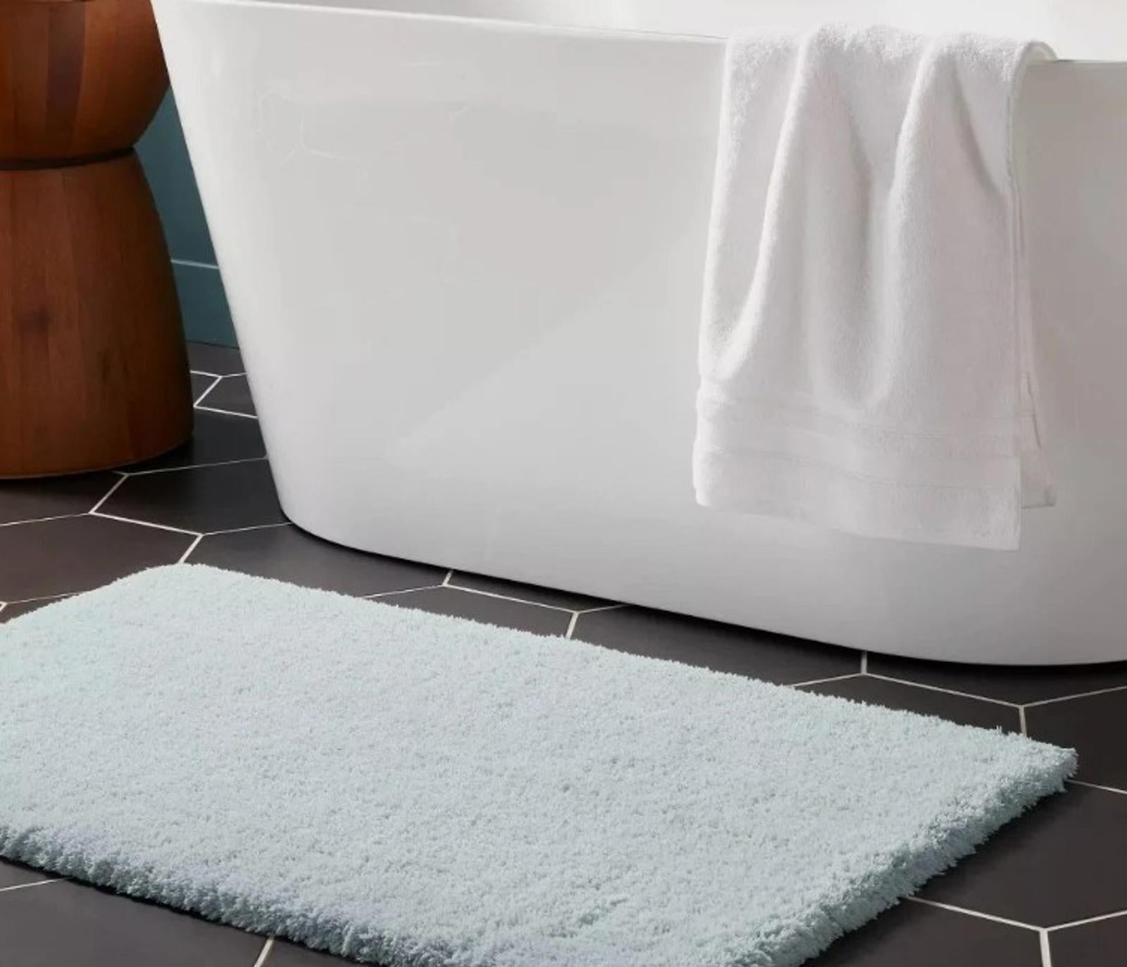 Soft blue bath mat placed in front of a modern bathtub, enhancing bathroom decor.