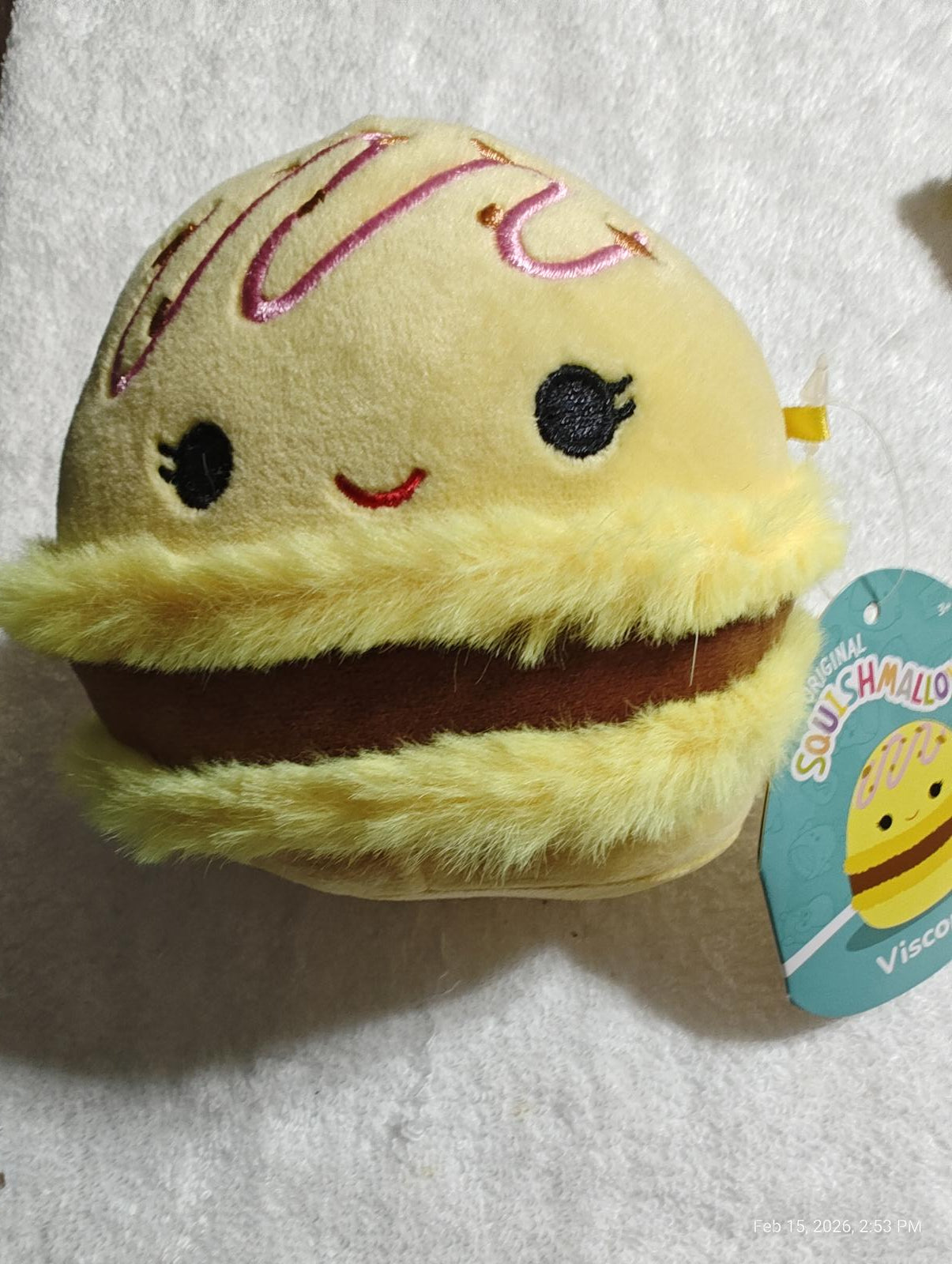 Squishmallow plush burger toy with yellow bun and brown filling, featuring cute facial expression.