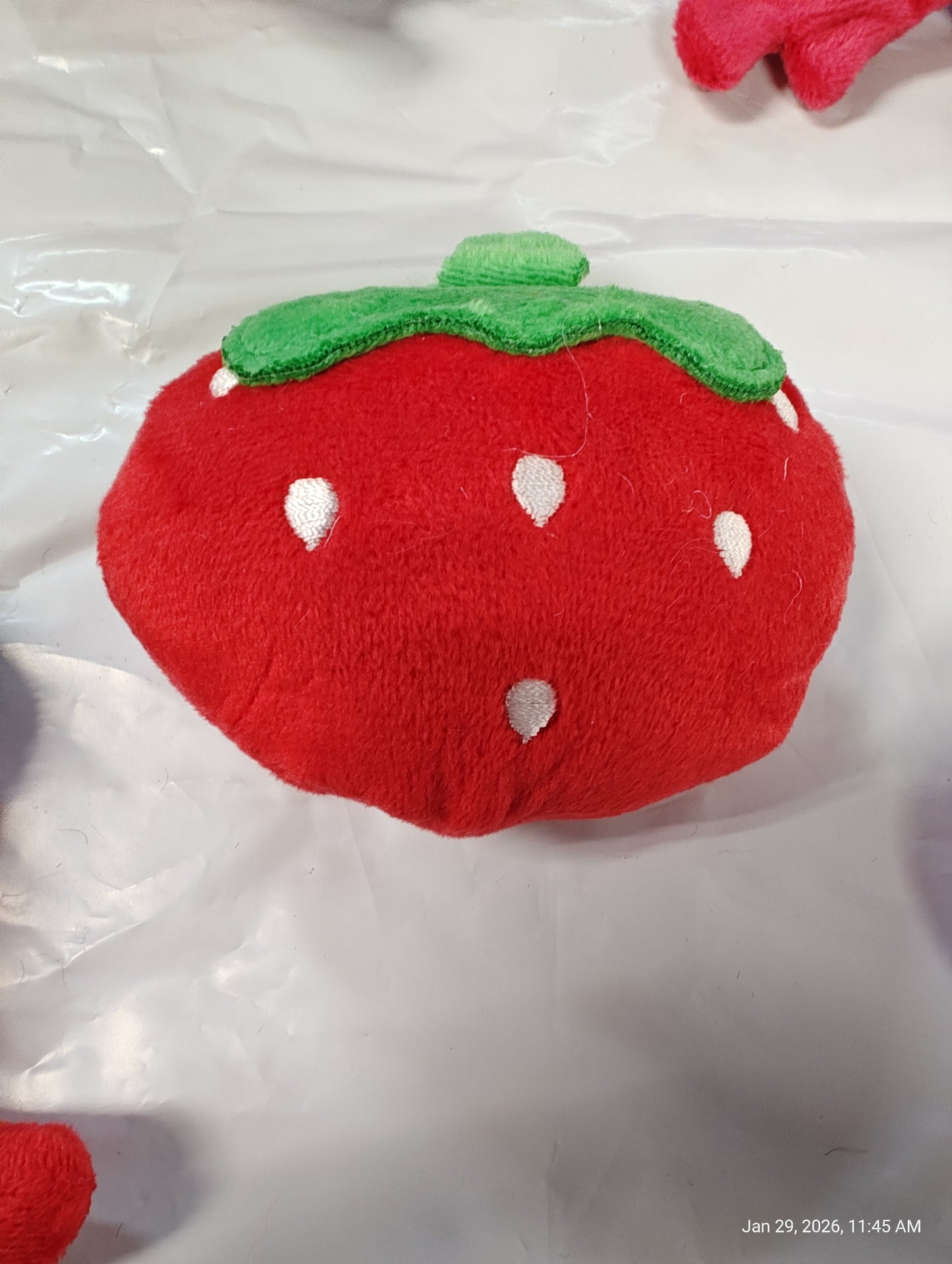 Strawberry plush toy with green leaves and white seeds, soft and cuddly.